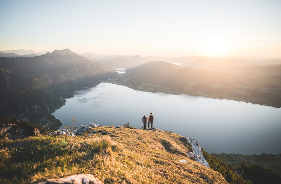 Zwei Wanderer genießen den Blick auf einen See in den Bergen bei Sonnenuntergang.