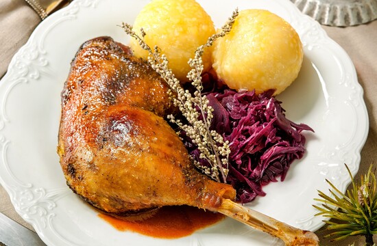 Gericht mit gebratener Gans, Rotkohl und Knödeln auf einem Teller, mit Soßenschüssel und Kerzenlicht auf einem weihnachtlich gedeckten Tisch.