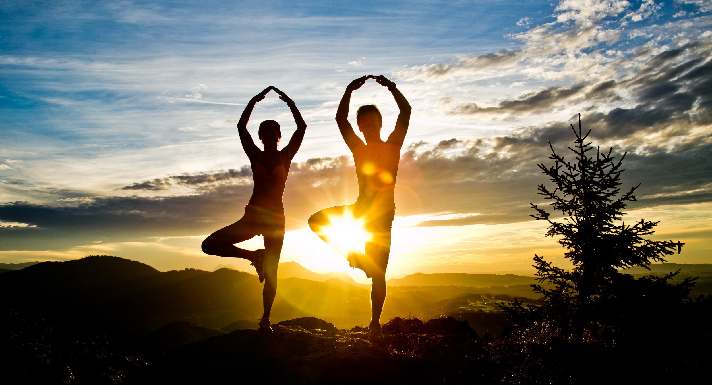 Ein Paar macht im Urlaub im Salzburger Land Yoga bei Sonnenuntergang