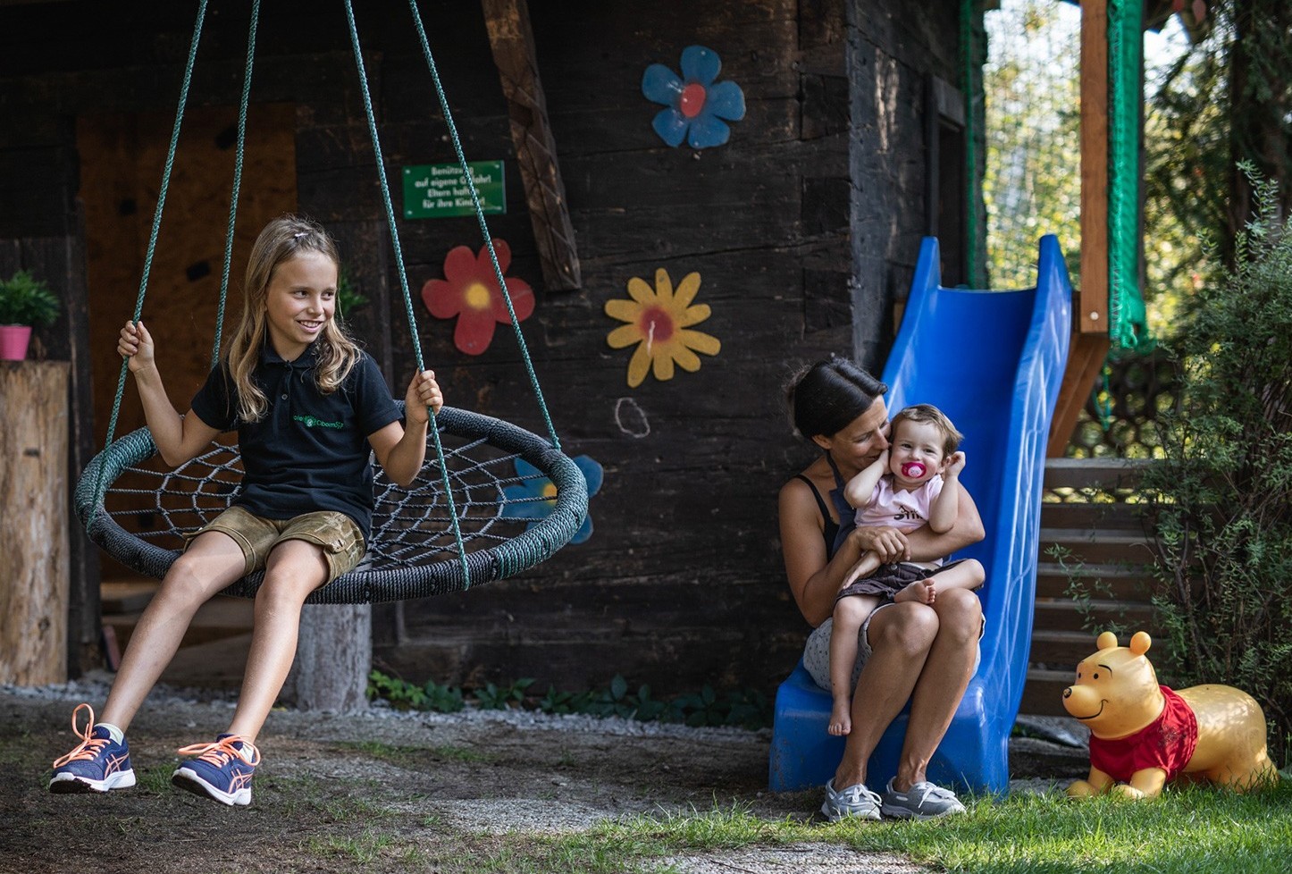 Eine Mutter spielt im Familienurlaub im Salzkammergut mit ihren zwei Töchtern am Spielplatz