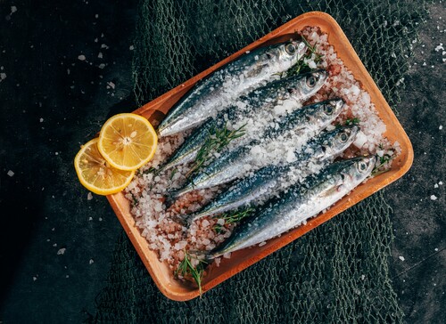 Frische Sardinen auf einem Holztablett mit Salz und Zitronenscheiben, dekoriert mit Kräutern.