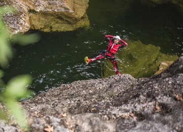 Eine Person in roter Ausrüstung entspannt beim Canyoning im Wasser in einer felsigen Umgebung.